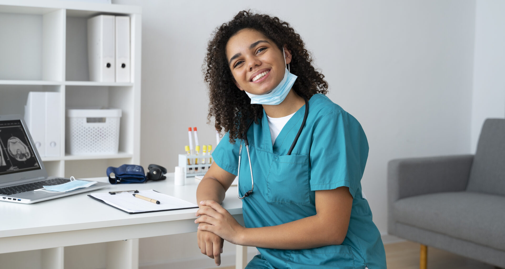 Remote healthcare professional in scrubs working from a home office with medical tools and a laptop