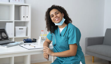 Remote healthcare professional in scrubs working from a home office with medical tools and a laptop