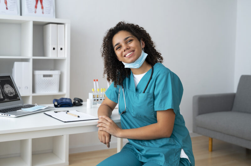 Remote healthcare professional in scrubs working from a home office with medical tools and a laptop