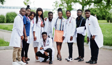 Group of diverse African medical students wearing white lab coats and stethoscopes, standing outdoors together, representing future doctors pursuing medical education and scholarship opportunities in 2026.