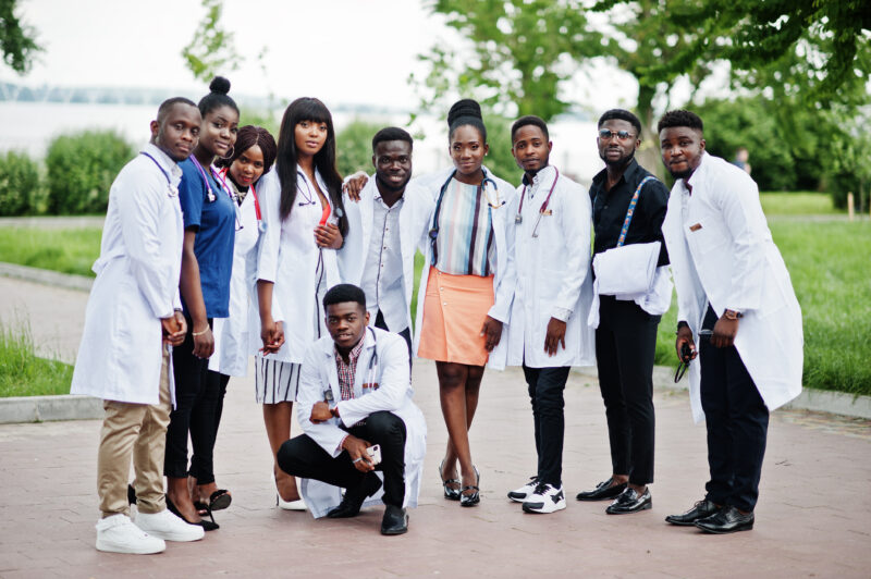 Group of diverse African medical students wearing white lab coats and stethoscopes, standing outdoors together, representing future doctors pursuing medical education and scholarship opportunities in 2026.