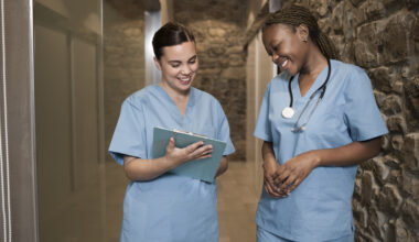Two registered nurses reviewing patient records in a hospital hallway during clinical practice training