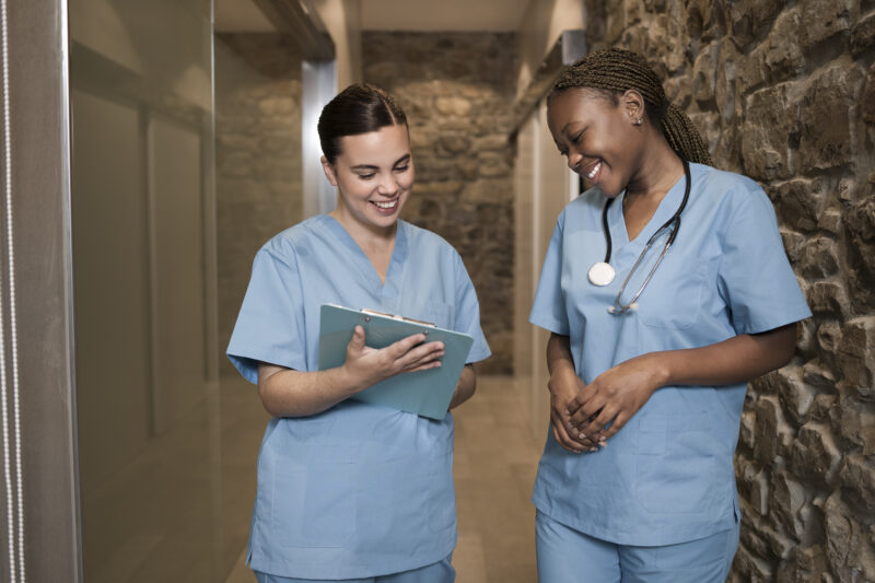 Two registered nurses reviewing patient records in a hospital hallway during clinical practice training