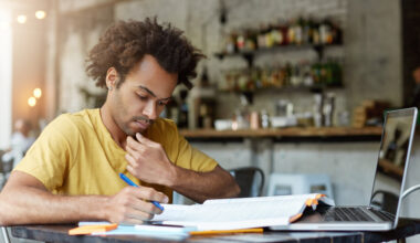 A student writing a scholarship essay on a laptop and notebook for university scholarship applications