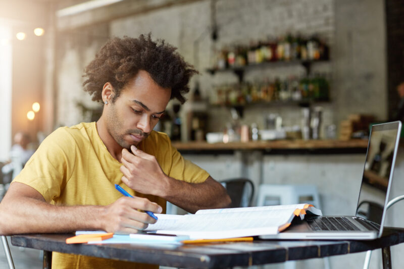 A student writing a scholarship essay on a laptop and notebook for university scholarship applications