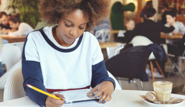 Student writing a Statement of Purpose for university admission using a tablet and notebook.