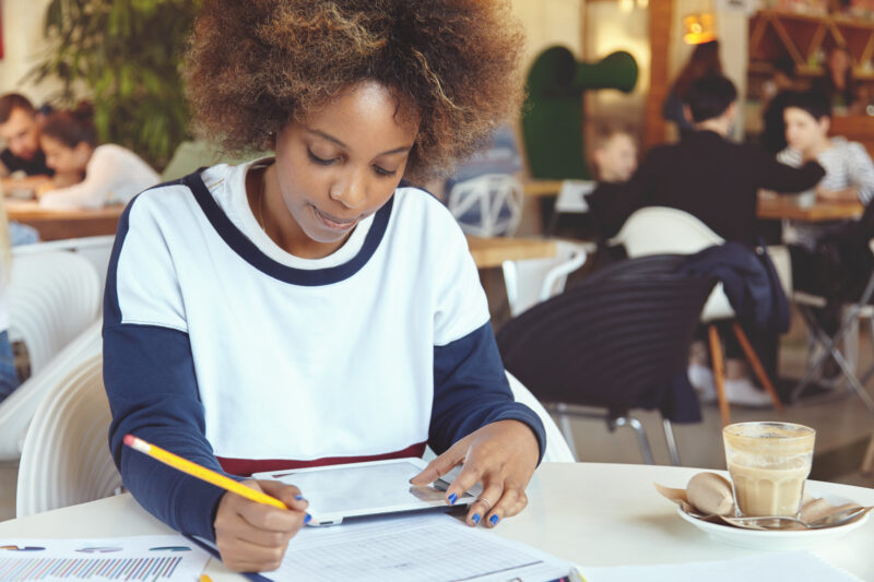 Student writing a Statement of Purpose for university admission using a tablet and notebook.